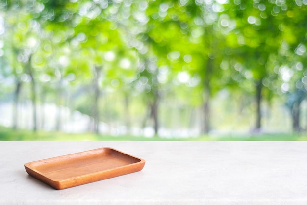 Leere Holzplatte auf weißem Tisch über unscharfer grüner Baumnatur mit Bokeh-Hintergrund