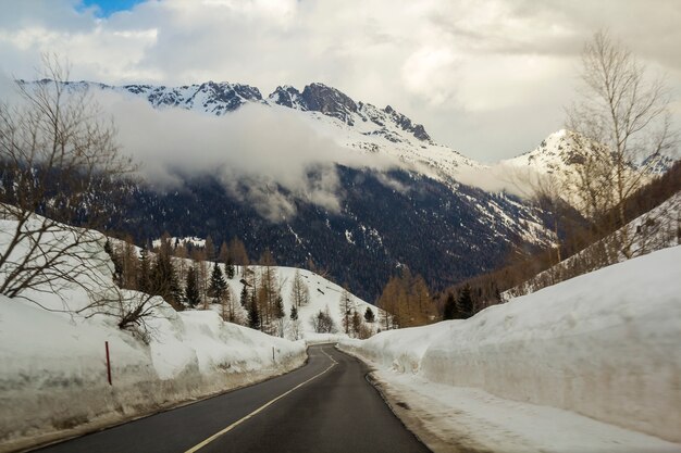 Leere kurvenreiche Asphaltstraße, die durch tiefen Schnee in Richtung zu den schönen hellen weißen Alpen ausdehnt