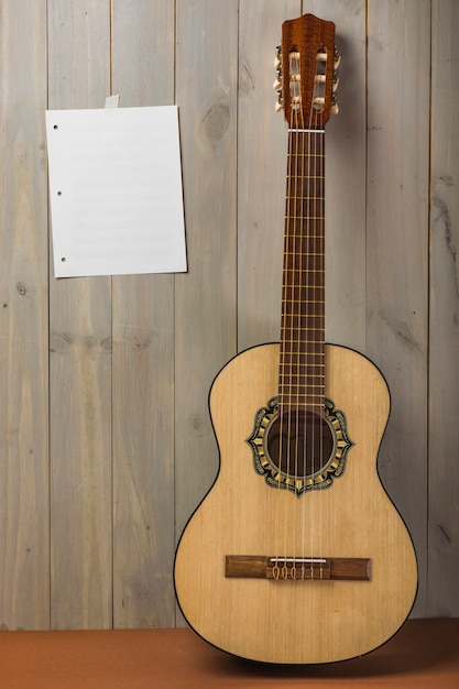 Leere musikalische Seite auf hölzerner Wand mit Gitarre