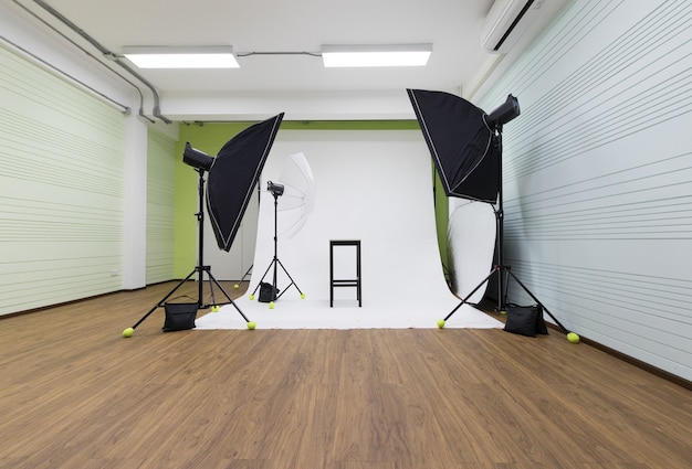 Leere Niemand Innenraum Studio weiße Fotoshooting-Szene mit professioneller Fotografenausrüstung Set Softbox Strobe Blitzschirm Reflektor Glühbirne auf Stativständer mit schwarzem Stuhl bereit für das Modell.