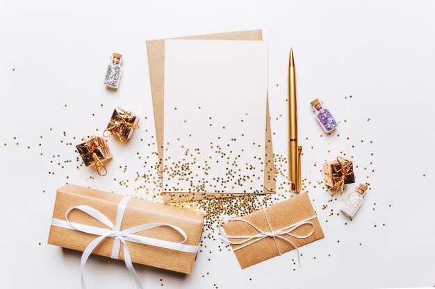 Leere Notiz mit Umschlag, Geschenken, Stift und Goldglittersternen auf weißem Hintergrund