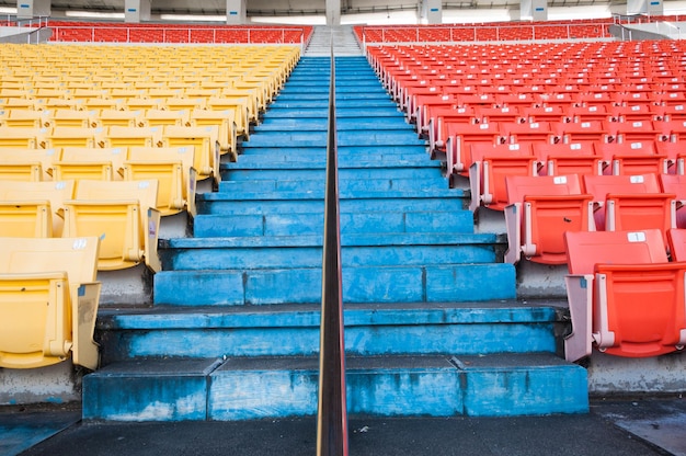 Leere orangefarbene und gelbe Sitze im StadiumRows-Gehweg mit Sitzplätzen in einem Fußballstadion