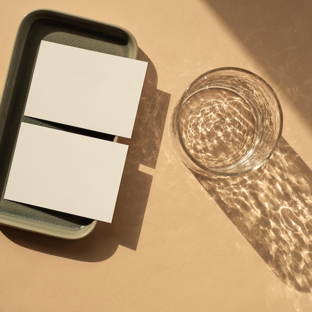 Foto leere papierblattkarte mit mockup-kopierbereich minimale luxuriöse ästhetische geschäftsmarkenvorlage glas mit sonnenlicht beschattet keramikplatten auf neutralem pfirsichfarbenem hintergrund flache ansicht von oben