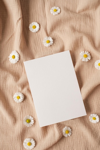 Leere Papierblattkarte mit Mockup-Kopierraum Kamillenblütenknospen und neutralem beigem Musselintuch Minimale ästhetische Hochzeitseinladungsvorlage Flache Ansicht von oben