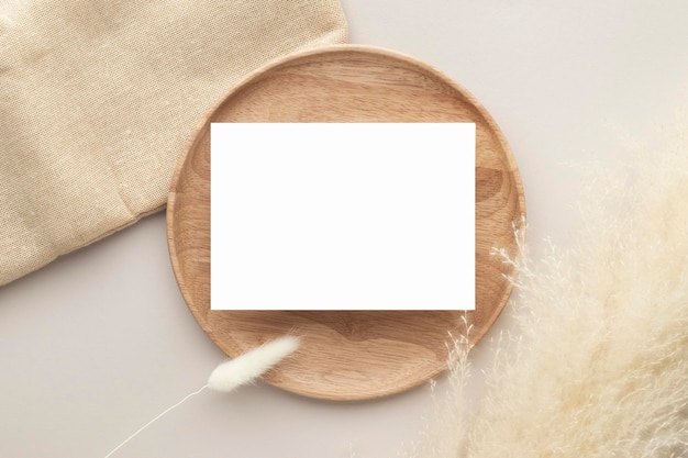 Leere Papierkarten, Mockup mit Pampasgras auf einer Holzplatte, beiger Hintergrund, minimale beige Arbeitsplatzzusammensetzung, flache Lage, Mockup