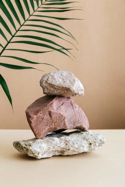 Leere Podium Stones Turm auf braunem Kraftpapier Hintergrund. Stones-Sockelanzeige auf beigefarbenem Hintergrund aus Muschelsteinen Palmblatt. Abstraktes Hintergrundmodell für die Produktpräsentation.