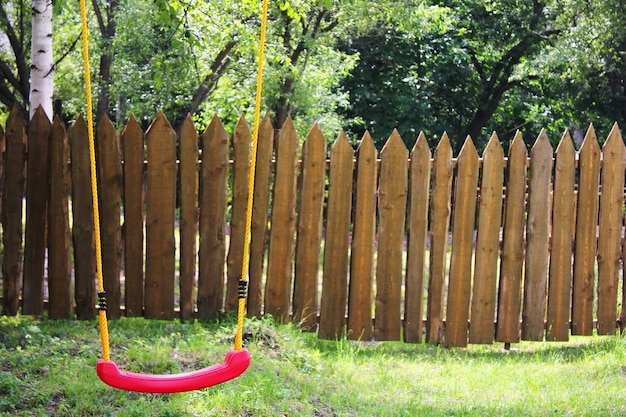 Leere rote Plastikschaukel der Kinder an gelben Seilen.