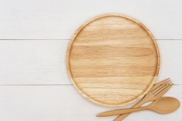 Leere runde Holzplatte mit Löffel und Gabel auf weißem Holztisch Draufsichtbild