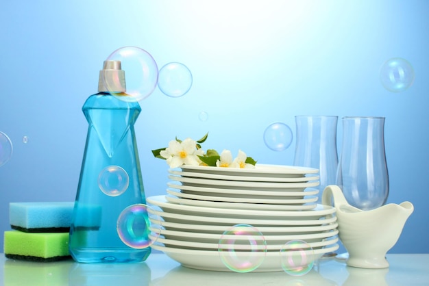 Leere saubere Teller und Gläser mit Spülschwämmen und Blumen auf blauem Hintergrund