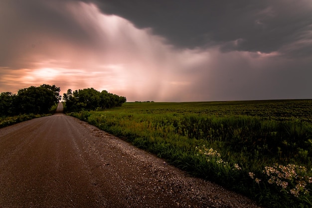 Leere Straße durch Feld gegen Sturmwolken beim Sonnenuntergang