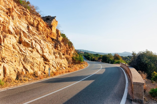 Leere Straße ohne Autos, auf der Insel Sardinien in Italien im Sommer. Panorama mit Autobahn und grüner Natur und blauem Himmel. Berge im Hintergrund.