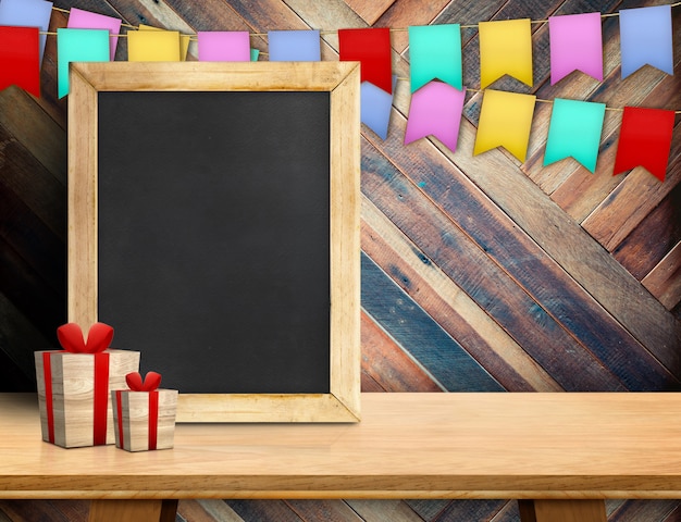 Leere Tafel mit Geschenkbox und bunten Flaggen auf Holz an der diagonalen hölzernen Wand. Exemplar