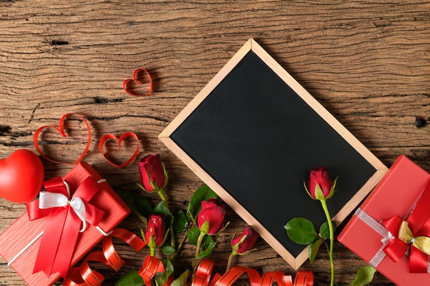 Leere Tafel mit roten Rosen und Herzband auf altem Holz