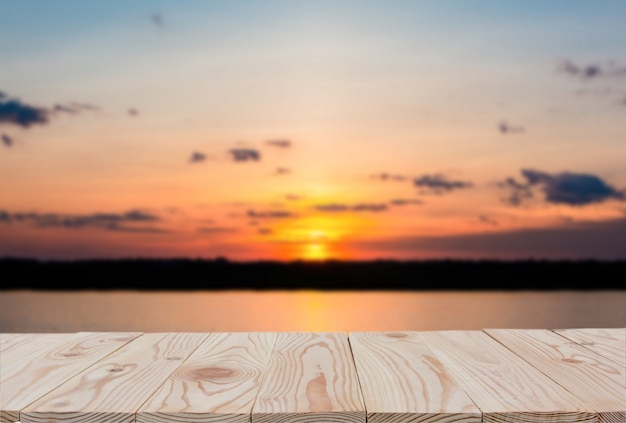 Leere Tischplatte des hölzernen Brettes an von unscharfem Sonnenuntergang- und Seehintergrund.