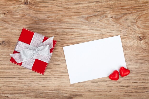 Foto leere valentinsgrußkarte und kleine rote geschenkbox auf holzuntergrund