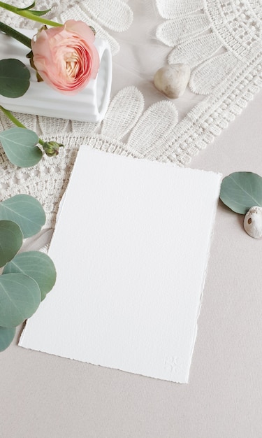 Foto leere weiße hochzeitsgrußeinladungskarte silber eukalyptusblätter zweig, erröten rosa butterblume ranunkelblume auf strukturiertem papiertisch backgound. elegante moderne vorlage flache draufsicht