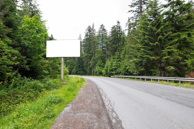 Leere weiße horizontale Plakatwand am Straßenrand Eine kurvige Straße zwischen dem Wald