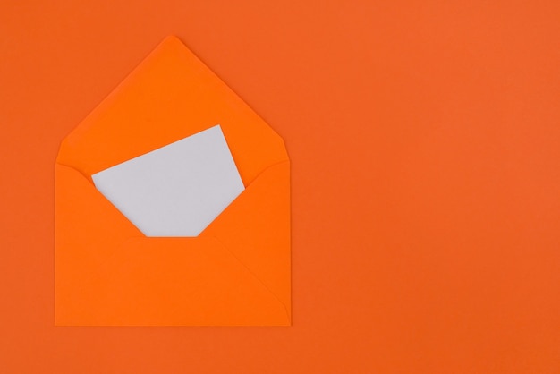Leere weiße Karte im orangefarbenen Umschlag lokalisiert auf pastellorangem Hintergrund mit Kopienraum.
