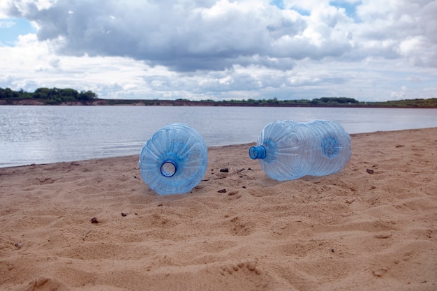 Leeren Sie benutzte schmutzige Plastikflaschen. Sandiges Ufer des schmutzigen Flusses. Umweltverschmutzung. Ökologisches Problem.