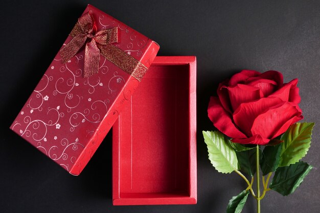 Leeren Sie rote Geschenkbox mit Rotrose auf schwarzem Hintergrund. Konzept von Valentinstag.