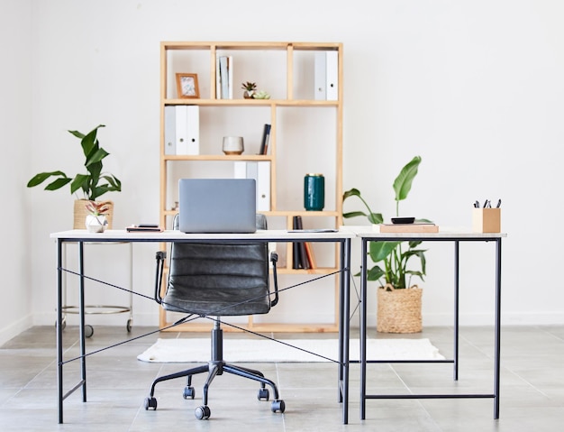Leerer Bürotisch oder Schreibtisch in einem Heimbüro oder Schreibtisch mit Stiften, Pflanzen oder Schreibwaren für die Produktivität Möbelstuhl oder moderner Büroraum mit Laptop oder Ordnern in einem Holzregal