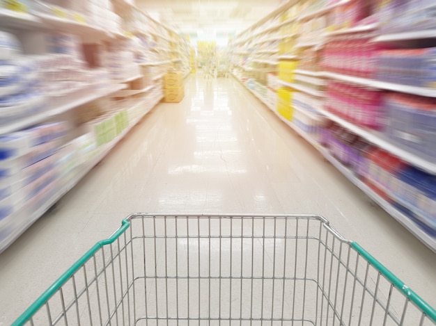 Leerer Einkaufswagen des Wagens auf der Insel mit Bewegungsunschärfe des Produktregals im Supermarkt