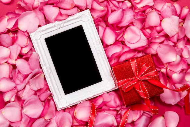 Leerer Fotorahmen mit süßem rosa Rosenblumenblatt und rote Geschenkbox, Romance und Liebeskartenkonzept