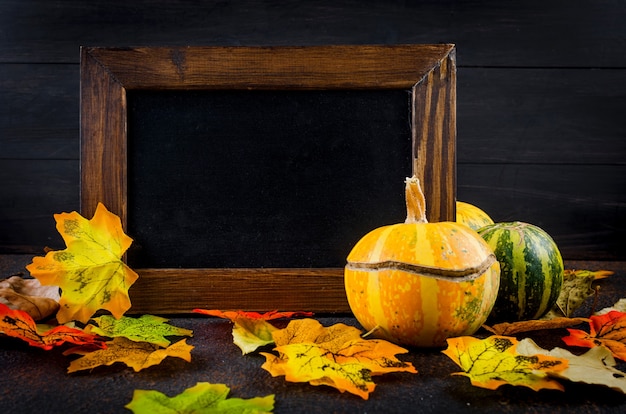 Leerer Holzrahmen, dekorative Mini-Kürbisse mit getrockneten Herbstblättern auf dunklem Betonhintergrund, Herbstkonzept, Kopienraum, Herbstkonzept oder Herbsturlaub, Erntedankfest, Kopienraum.