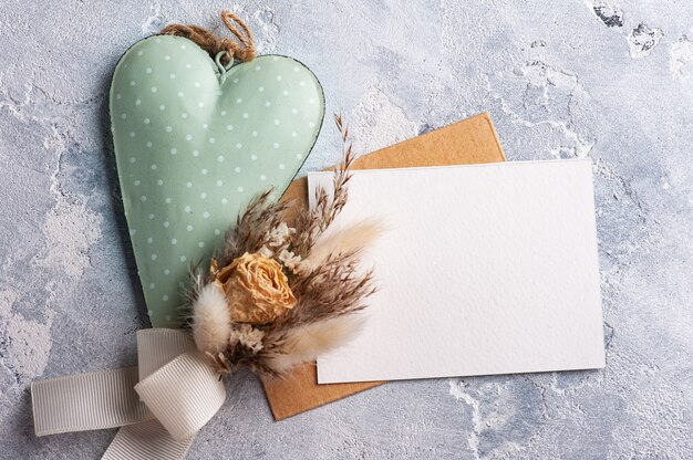 Foto leerer kraftumschlag mit strauß trockener blumen und grünem herzen. hochzeitsmodell auf grauem tisch