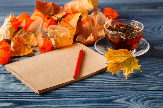 Leerer Notizblock und bunte Herbstahornblätter auf hölzernem Tischhintergrund
