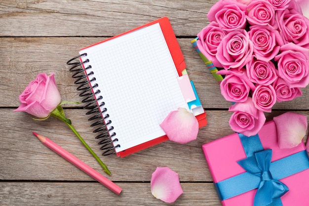 Leerer Notizblock und Geschenkbox voller rosa Rosen