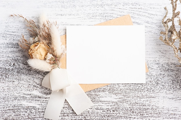 Leerer papier- und kraftumschlag mit neutralem blumenstrauß aus trockenen blumen. hochzeitsmodell auf weißem tisch