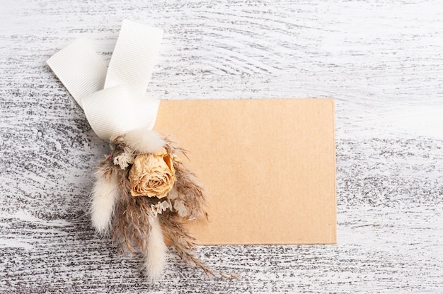 Leerer Papier- und Kraftumschlag mit neutralem Blumenstrauß aus trockenen Blumen. Hochzeitsmodell auf weißem Tisch