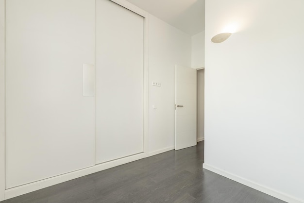 Leerer Raum in einem Haus mit grauem Laminatboden, weiß gestrichenen schlichten Wänden und weiß lackierten Holzschiebetüren