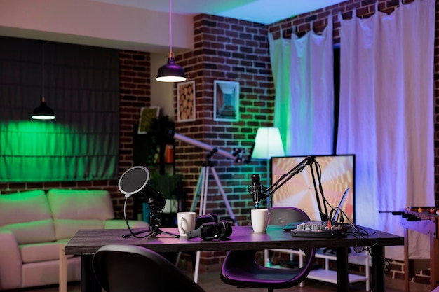 Leerer Schreibtisch im Heimproduktionsstudio mit Podcast-Ausrüstung, Technologie zur Aufnahme von Sound für die Produktion von Social-Media-Kanälen. Live-Sendungsraum im Wohnzimmer mit Neonlichtern