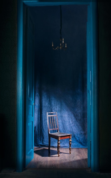 leerer Stuhl im Licht hinter blauen massiven Vintage-Türen im Innenbereich Altmodisches Innenkonzept