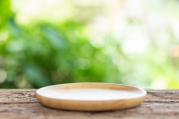 Leerer Teller auf Holztisch mit grünem Unschärfelichthintergrund. Für die Fotomontage