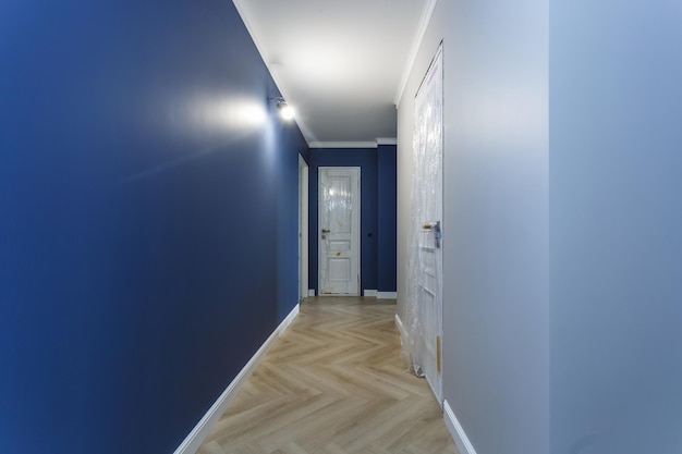 Leerer, unmöblierter Korridor mit minimalen vorbereitenden Reparaturen mit Zierleisten im Inneren aus weißen und blauen Wänden