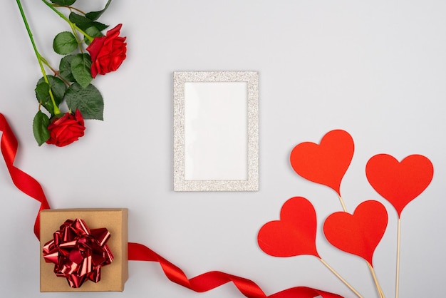 Leerer weißer Rahmen mit roten Rosen mit Craft-Papier Geschenkkiste rote Herzen mit Stick rotem Band