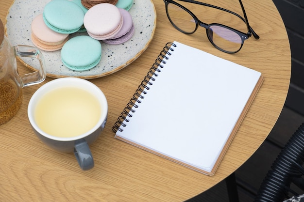 Leerer Zettel mit einer Tasse Tee und Macarons auf dem Café-Tischhintergrund. Geschäft im Cafeteria-Konzept