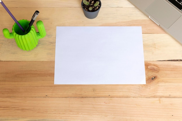 Leeres A4-Papier, das horizontal auf einem Holztisch mit Zubehör liegt