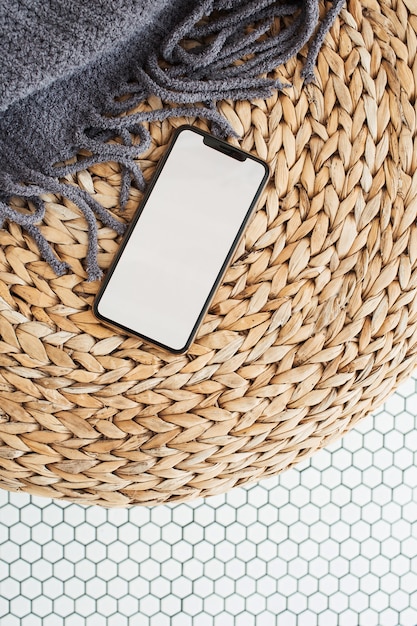 Leeres Bildschirm-Smartphone mit leerem Kopierplatzmodell auf Rattan-Puff, Plaid und Mosaikfliese
