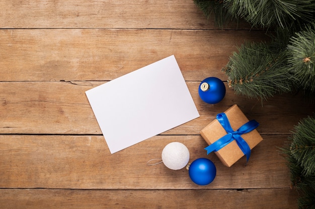 Leeres Blatt Papier und ein Geschenk unter dem Weihnachtsbaum auf einem hölzernen Hintergrund. Ansicht von oben, flach.