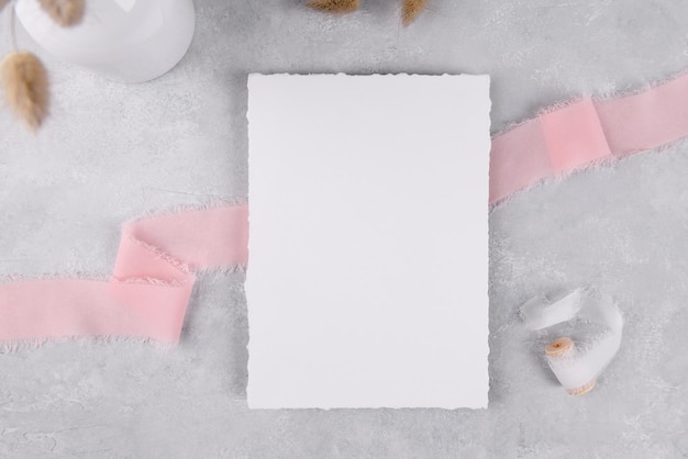 Leeres Briefpapier-Kartenmodell der Hochzeitseinladung auf grauem Steintischhintergrund mit rosa Schleife, 5x7