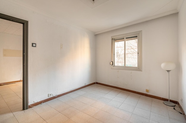 Leeres, geräumiges Zimmer mit Fenster und schmutzigen Wänden in einer alten Wohnung vor der Renovierung