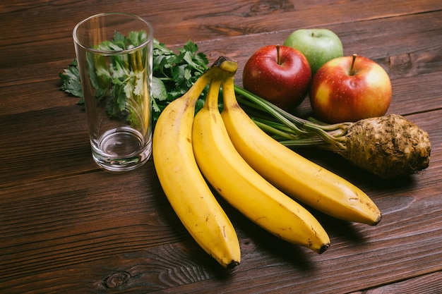 Leeres Glas, Äpfel, Selleriewurzel und Bananen auf einem dunklen Holztisch