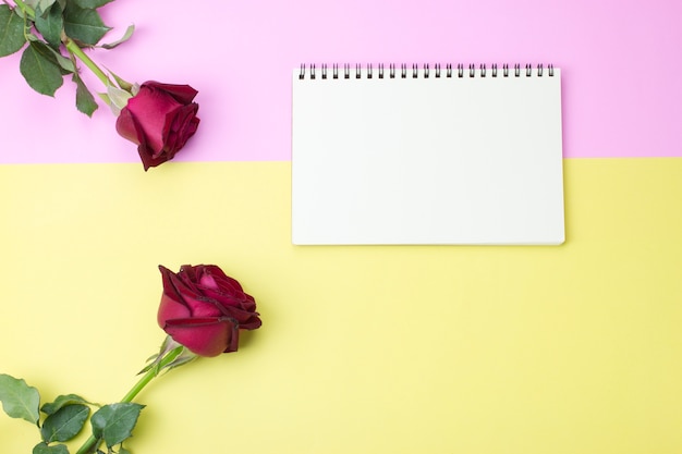 Leeres Notizbuch auf rosa und gelbem Papier mit Rosen, flache Lage, Draufsicht.