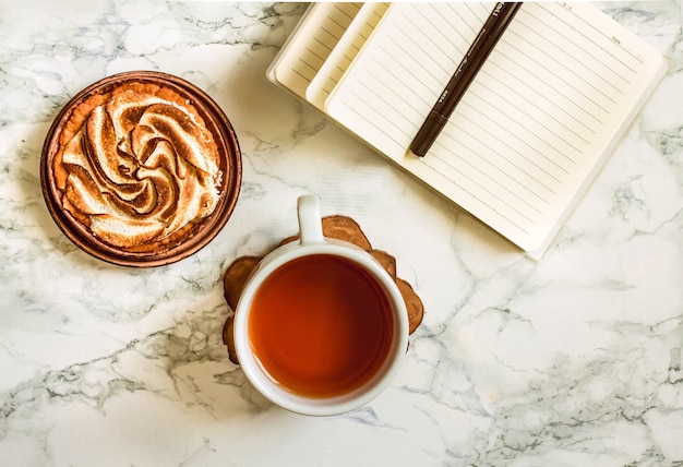 Leeres Notizbuch, eine Tasse Tee und Kuchen. Draufsicht mit Kopienraum. Arbeitsplatz. Planungskonzept.