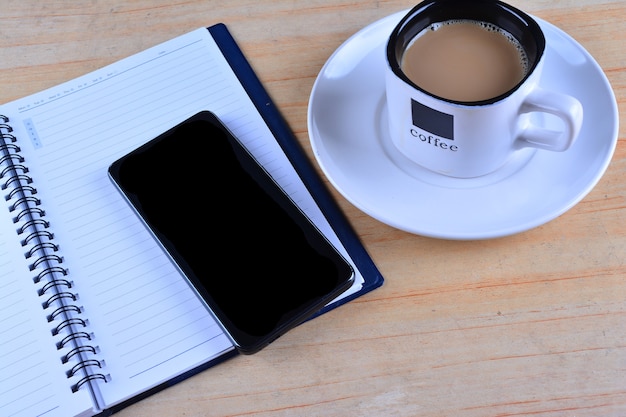 Leeres Notizbuch, Füllfederhalter, Smartphone und Tasse Kaffee auf dem Schreibtisch