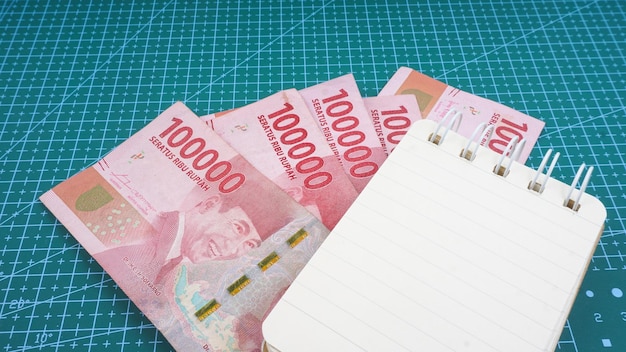Leeres Notizbuch mit indonesischem Geld auf grünem Gitterhintergrund